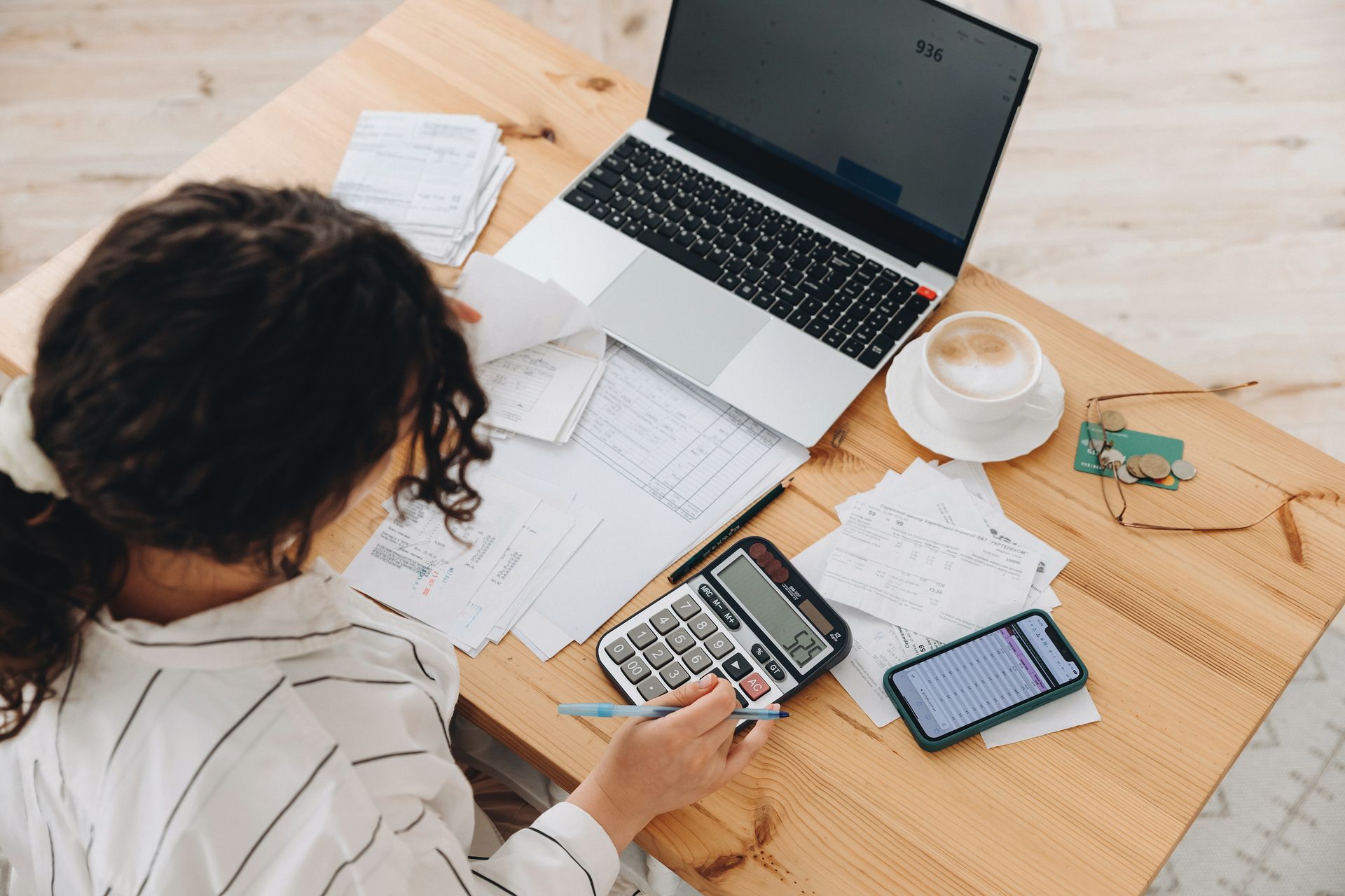 Person working at a desk with a laptop, phone, coffee, and papers spread out. Person working at a desk with a laptop, phone, coffee, and papers spread out.