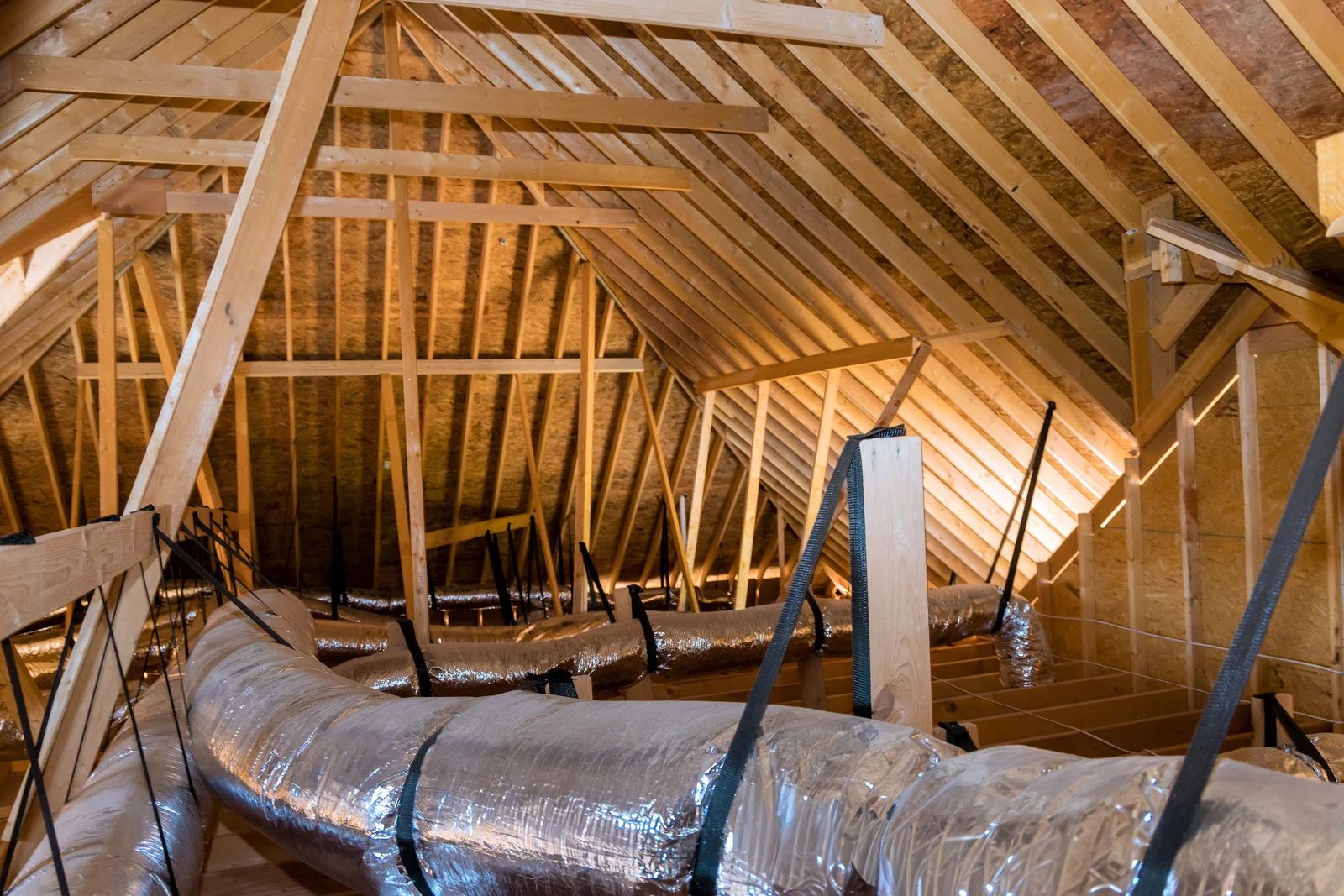Unfinished attic with exposed wooden rafters and insulated ductwork under construction.