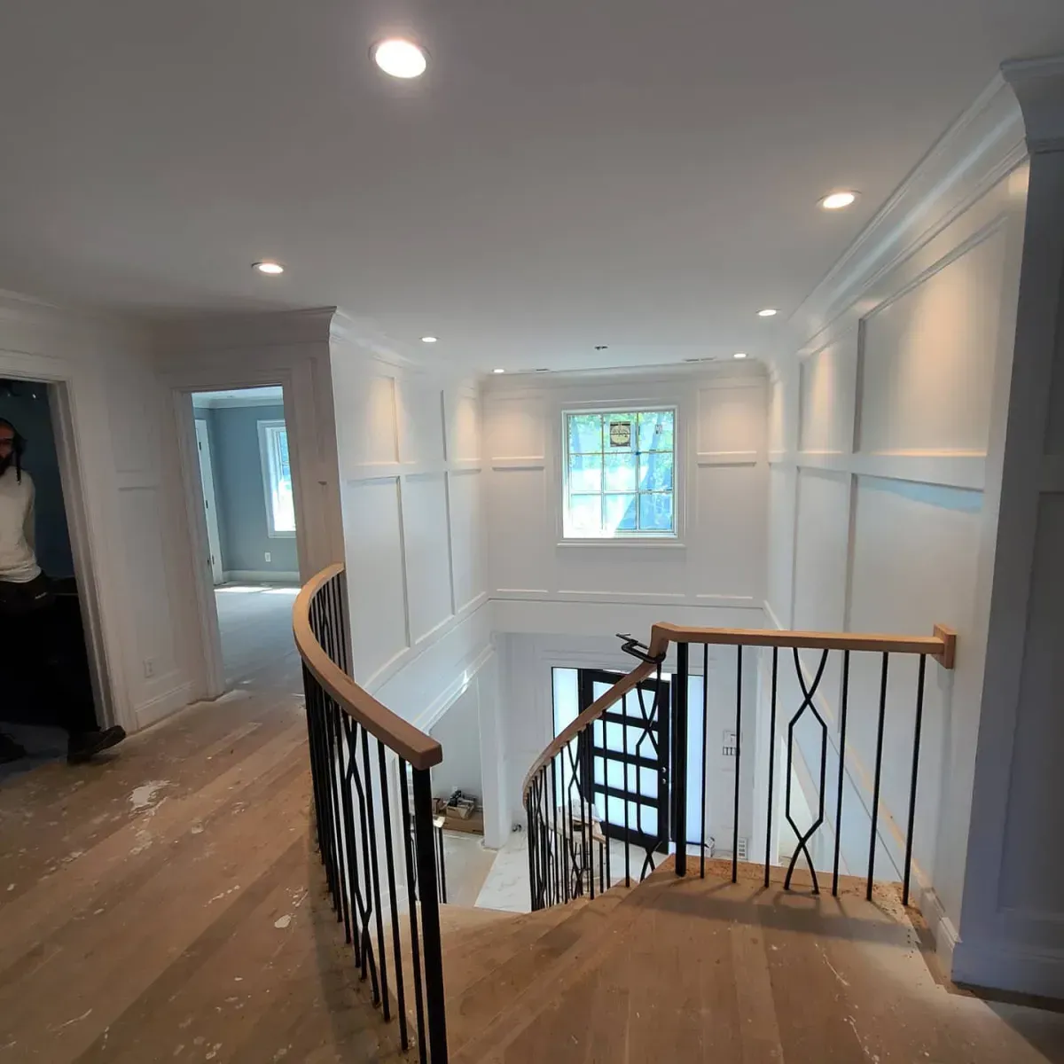A man is standing in a hallway next to a staircase in a house.