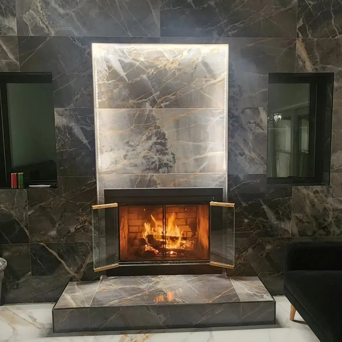 A fireplace in a living room with a marble wall and a couch.