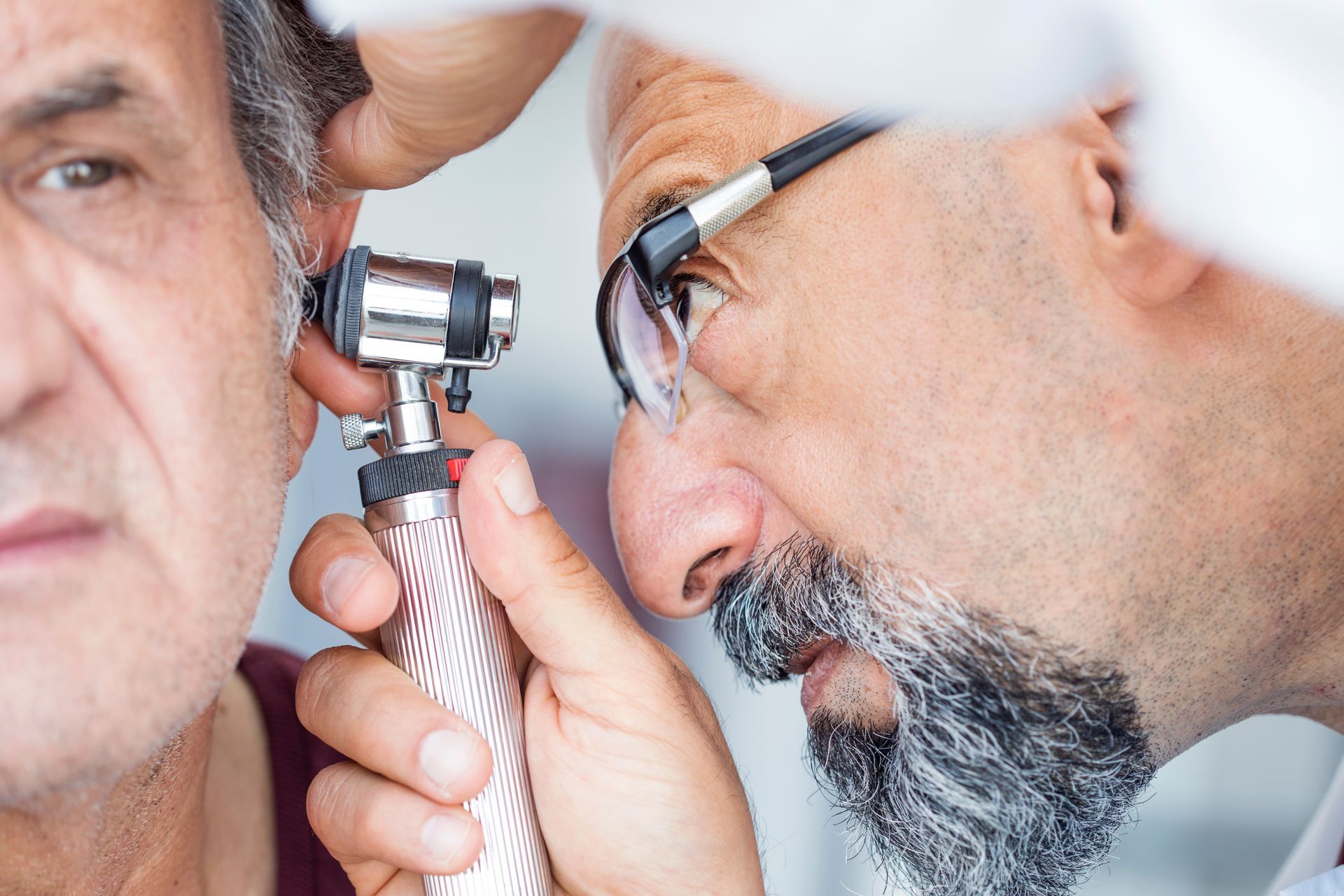 Local audiologist using an otoscope to examine an older man's ear during a routine hearing checkup. Local audiologist using an otoscope to examine an older man's ear during a routine hearing checkup.