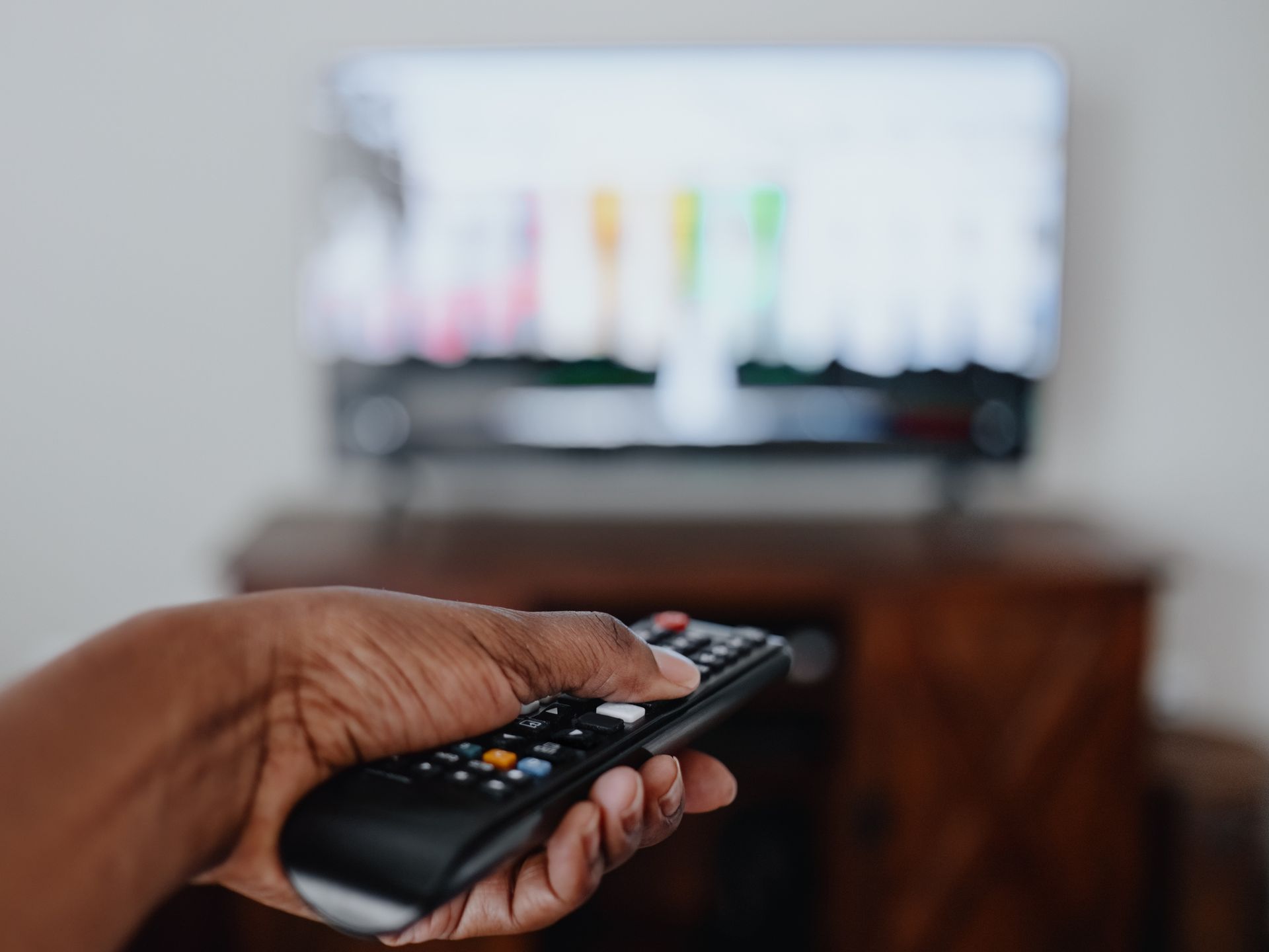 A hand holding a remote control, pointed toward a blurred television screen.