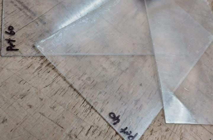 Plantillas de plástico transparente sobre una superficie de madera, con anotaciones manuscritas y bocetos a lápiz.