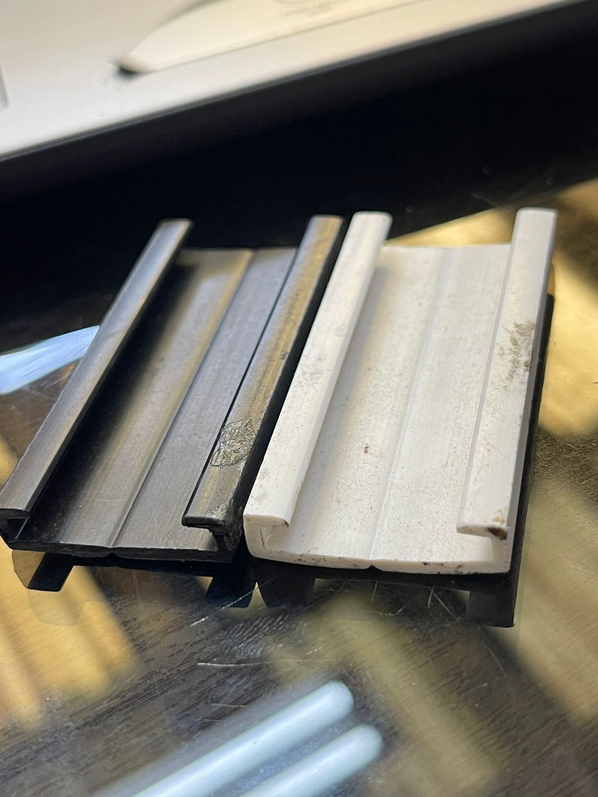 Primer plano de dos tiradores metálicos para cajones, uno negro y otro plateado, sobre una superficie reflectante.
