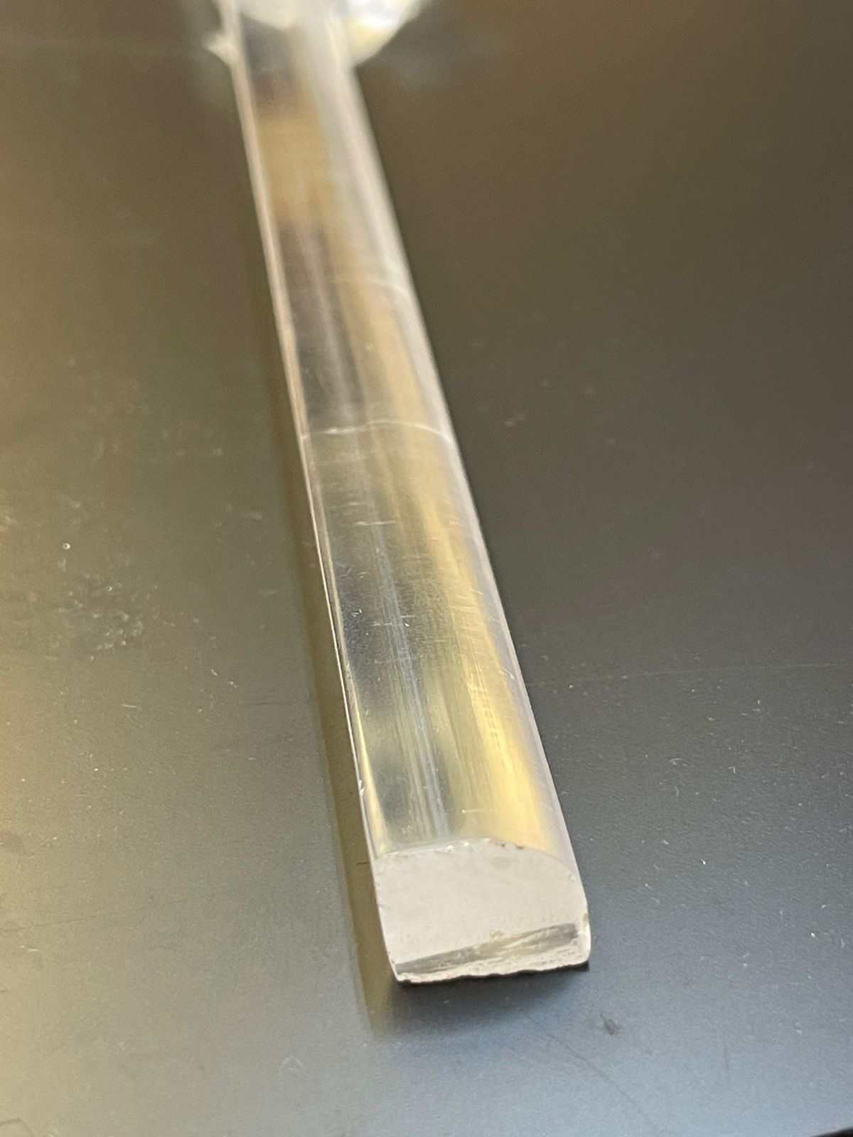 Tubo de plástico transparente sobre una superficie oscura, que muestra un extremo blanco cortado de forma irregular.