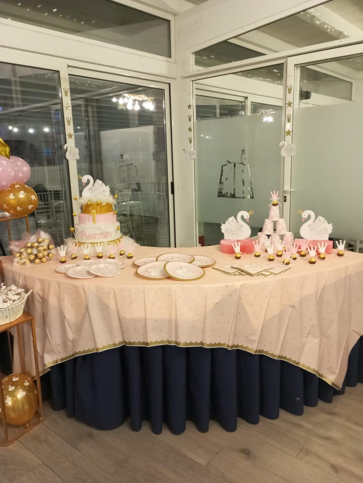 Un tavolo con una tovaglia rosa e una gonna blu è decorato con cigni e palloncini.