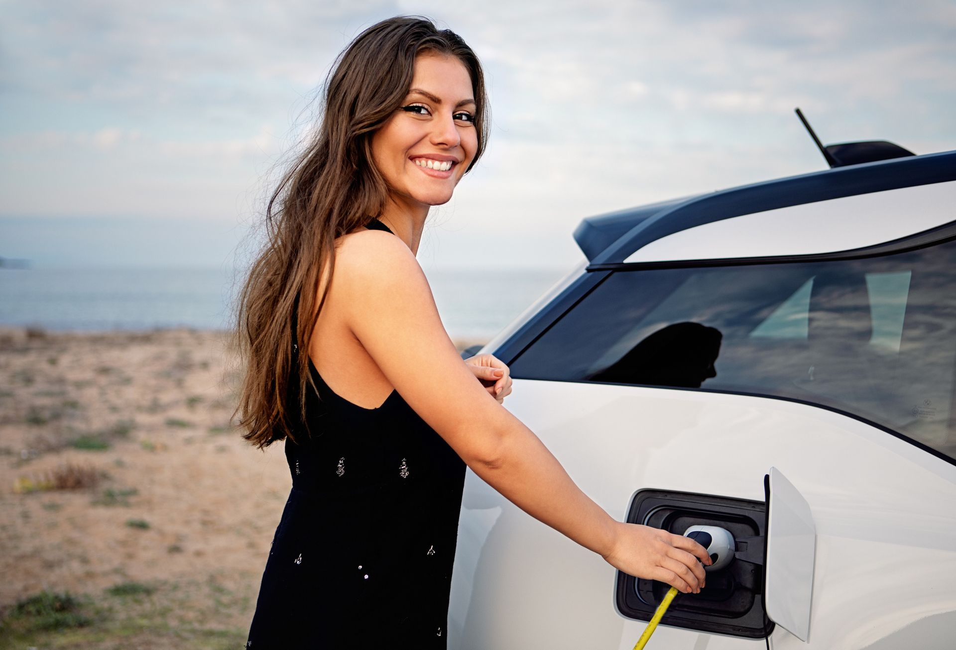 Una donna sta ricaricando la sua auto elettrica sulla spiaggia.