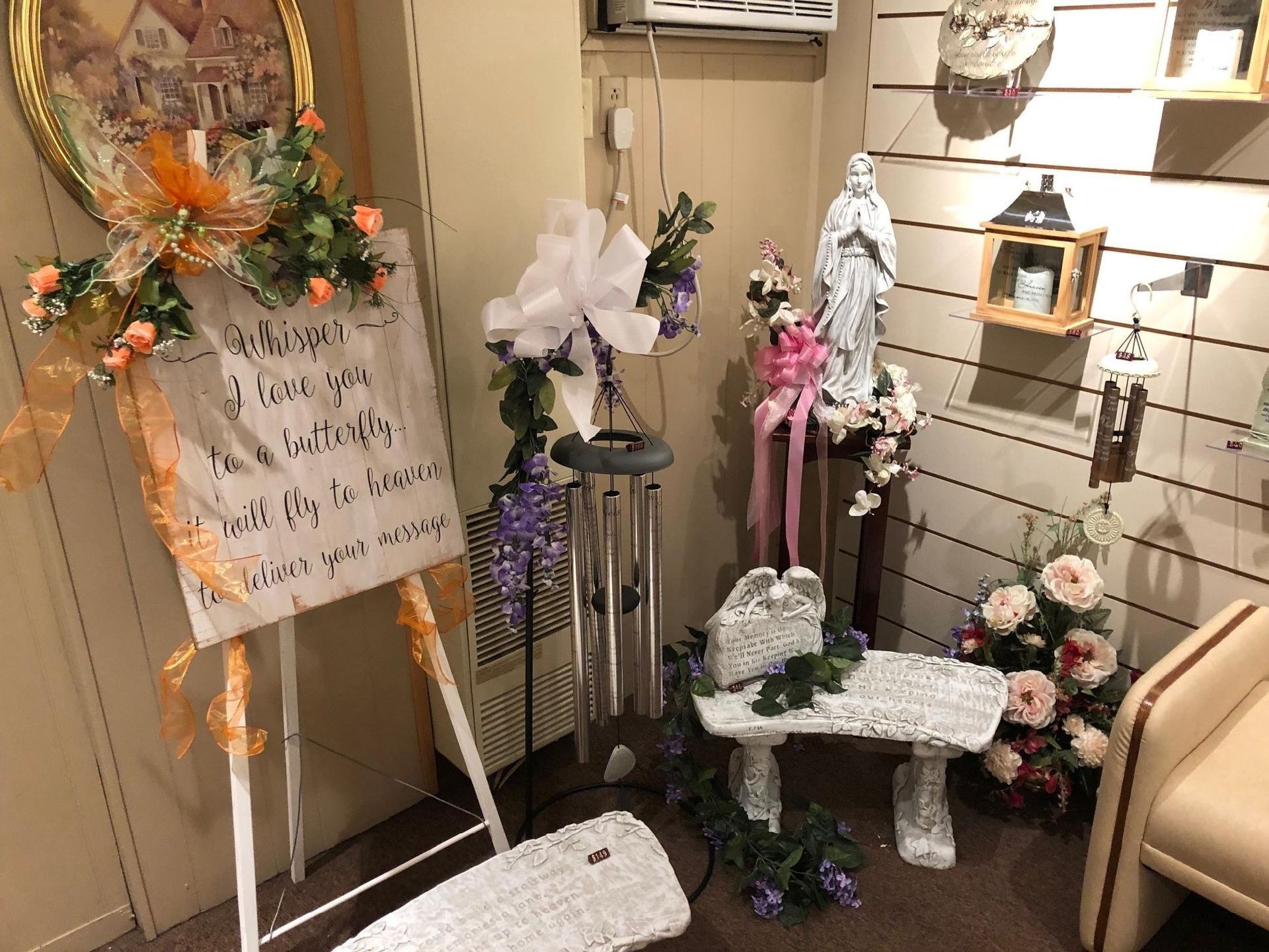 Decorated memorial display with flowers, handwritten sign, and white cross near a chair indoors