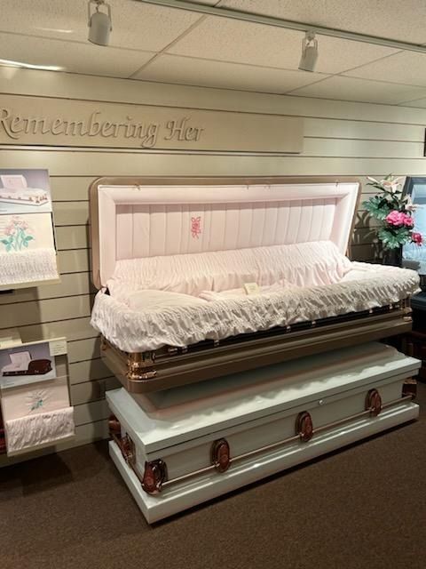 White casket with pink lining and white ruffled trim displayed in a funeral home showroom