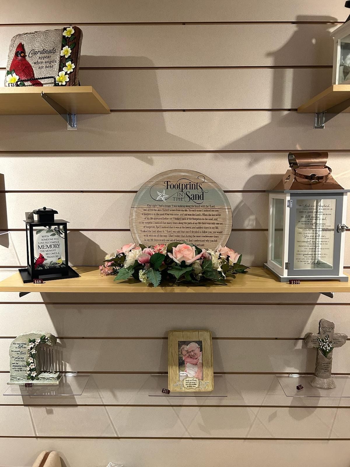 Shelves displaying memorial plaques, flowers, and framed keepsakes on a slatwall display.
