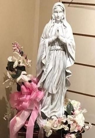 White Virgin Mary statue with pink and white flowers and ribbon decoration in a chapel alcove