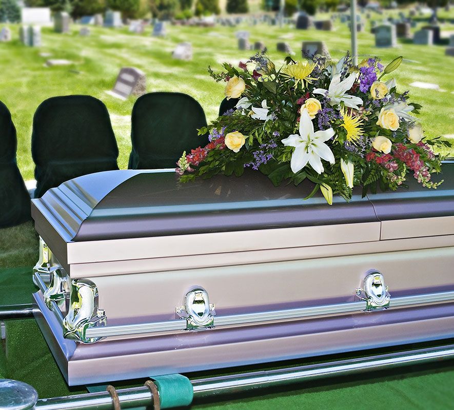 Silver casket with floral arrangement at an outdoor graveside service
