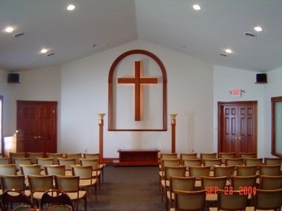 Interior of a chapel with rows of chairs facing a wooden cross on a wall.