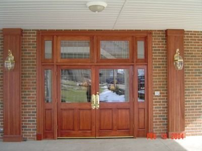Wooden double doors with sidelights and transom, brick wall, outdoor setting.