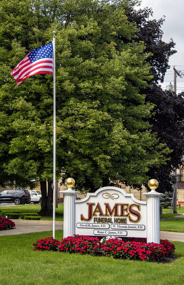 Sign for James Funeral Home; white with gold accents, floral border.