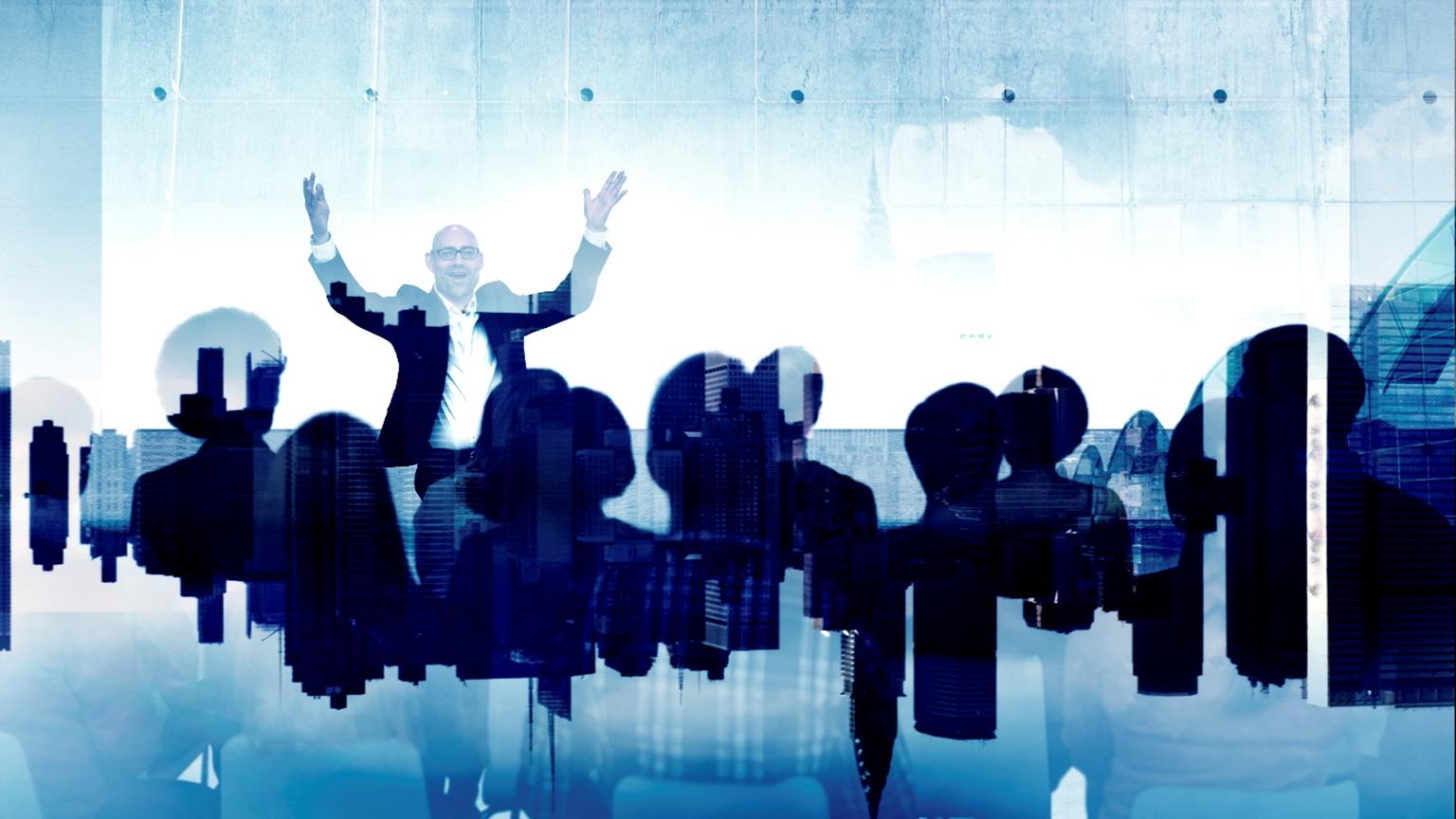 CEO leader in front of his employees with his arms raised in the air smiling.