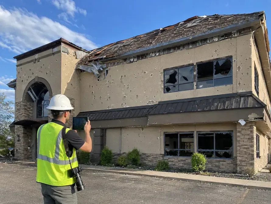 Forensic engineer documenting storm-related structural damage at a residential property while reviewing evidence for an insurance claim investigation.
