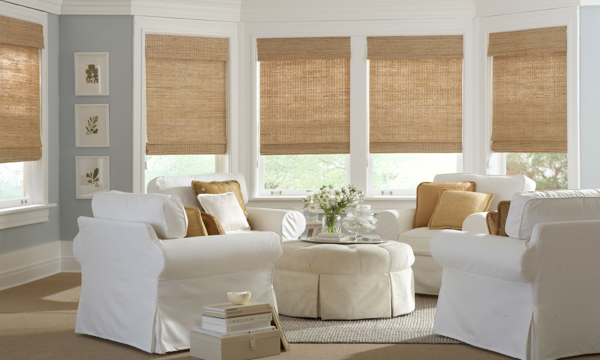 A bright living room with white slipcovered furniture, natural woven shades, and light blue walls.