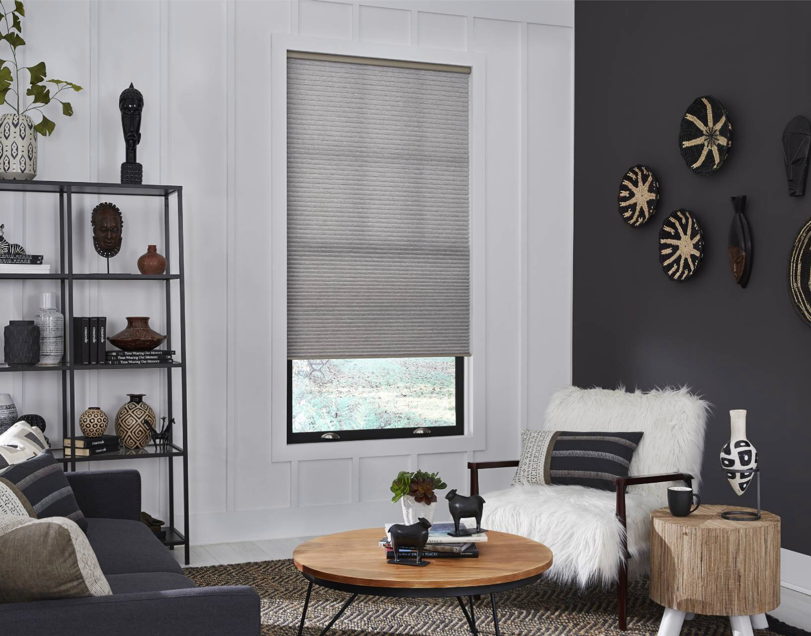 Living room with dark gray sofa, round wooden coffee table, window with shade, decorative wall hangings.