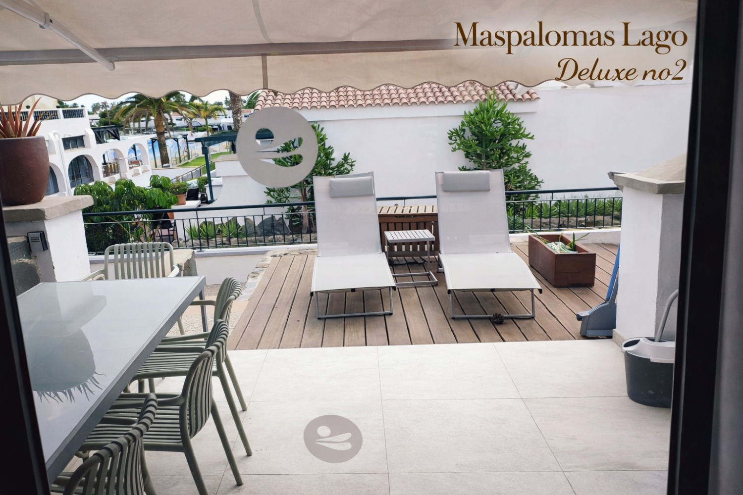 A balcony terrace with outdoor chairs, a table, and two lounge chairs, overlooking a resort area.