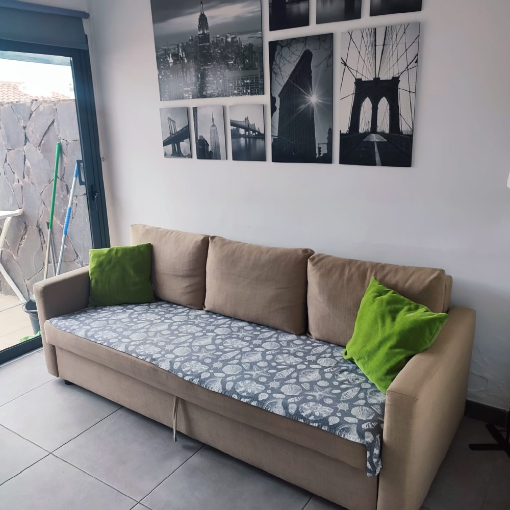 A beige sofa with a patterned cover and two green pillows, placed against a wall featuring black and white city prints.