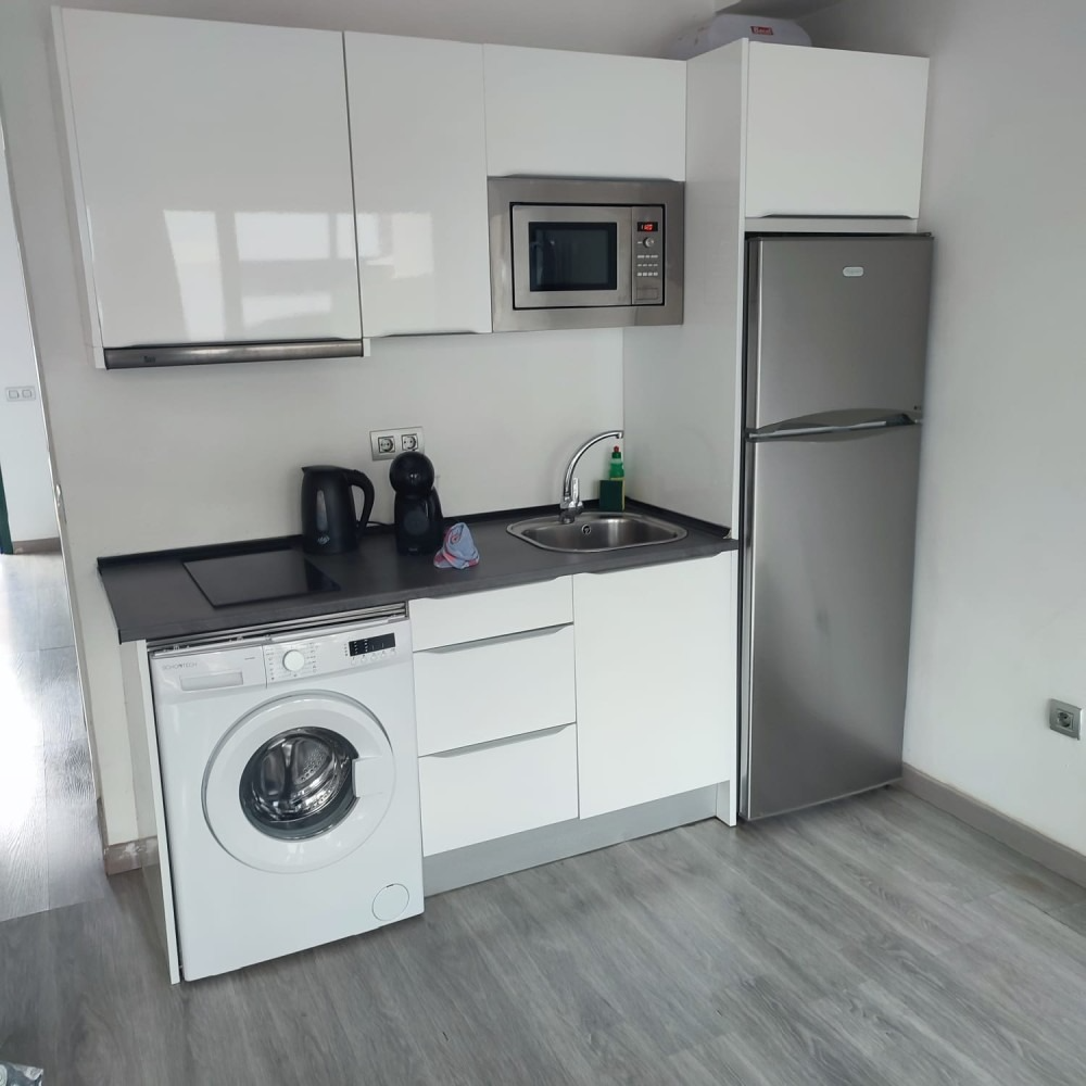 A modern small kitchen with white cabinets, a silver refrigerator, a built-in microwave, and a white washing machine.