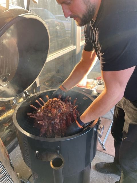 A man is cooking meat on a grill with the lid open