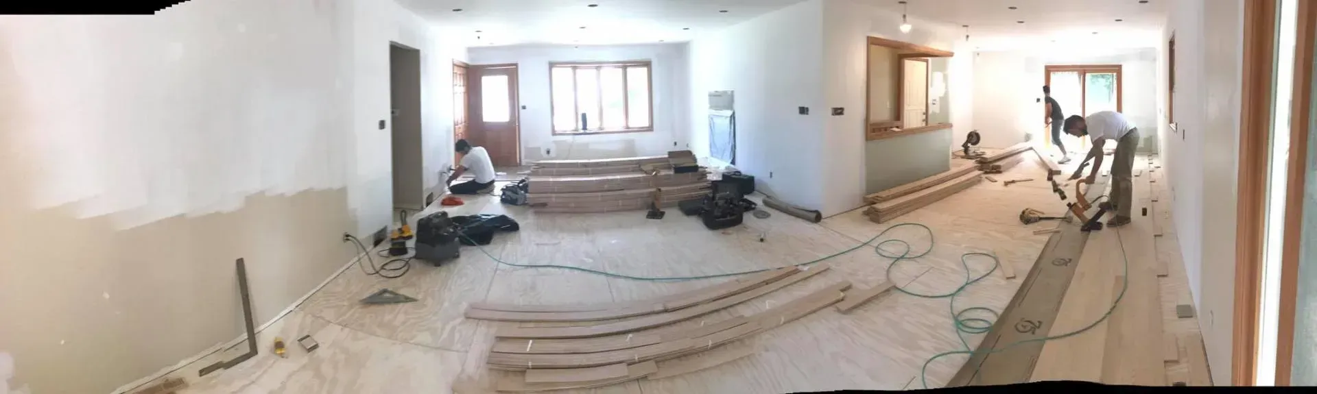 Interior renovation in progress; workers install wood flooring.