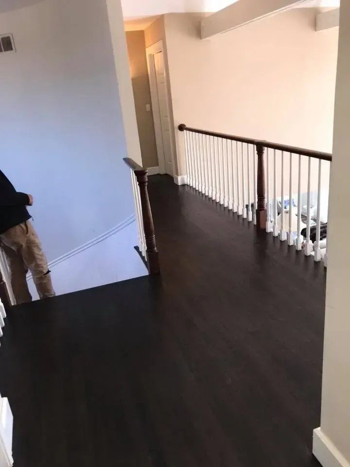 Hallway with dark wood flooring, white banister with wooden handrail.