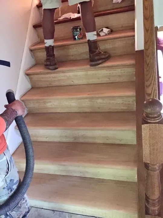 Person vacuuming wooden stairs, another standing on the top steps.