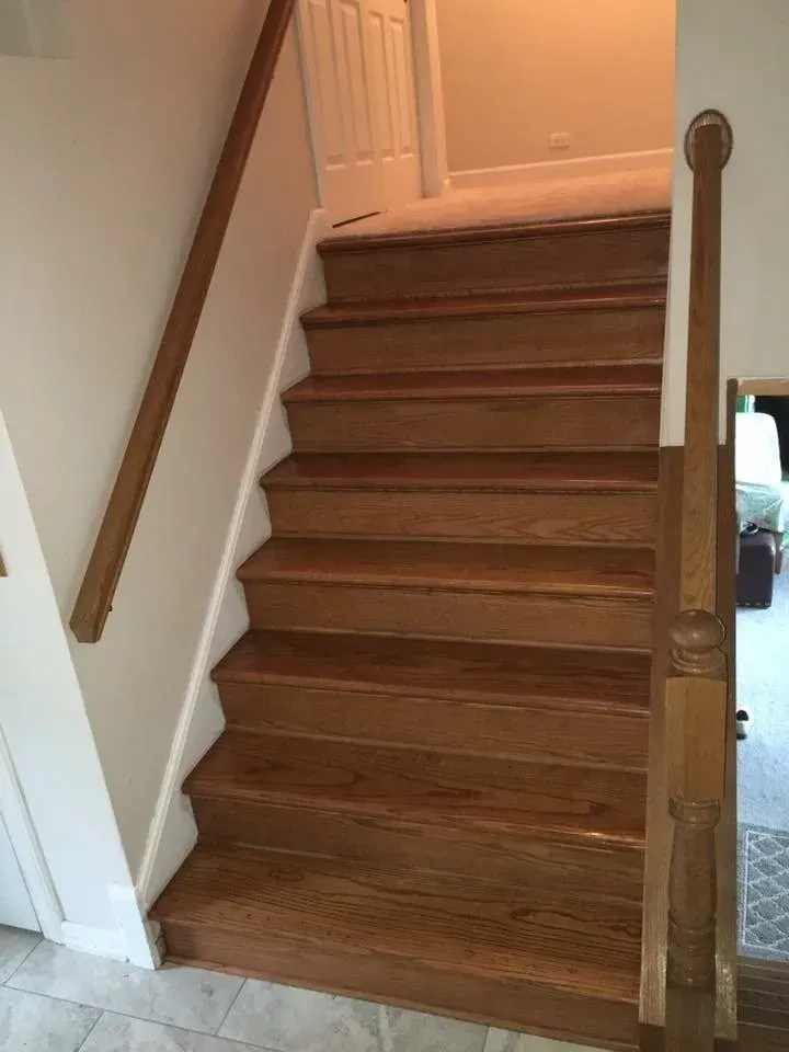 Wooden staircase with a handrail, leading upwards, with white walls and a door at the top.