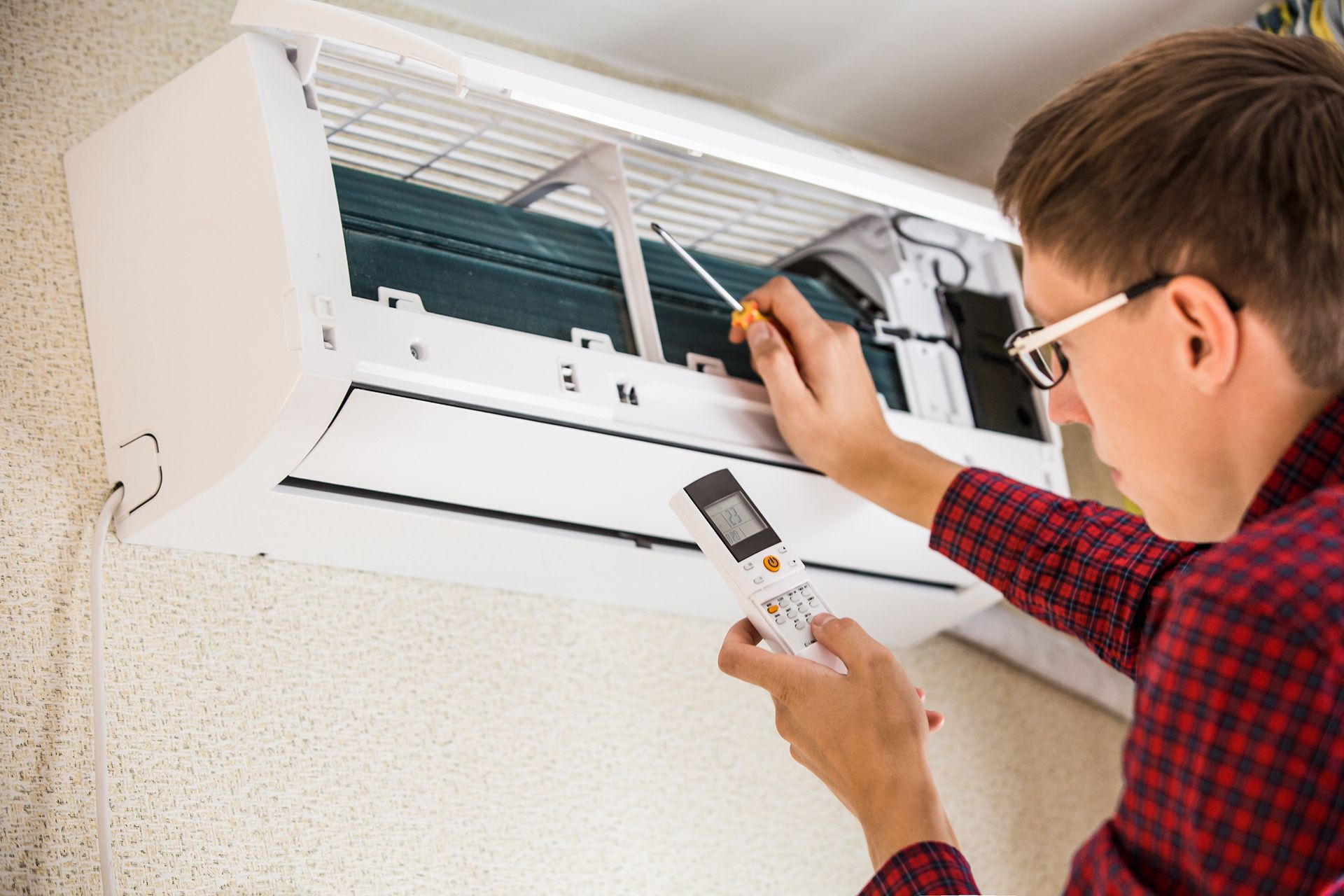 A technician is testing a wall-mounted unit with a remote for a professional AC repair company. A technician is testing a wall-mounted unit with a remote for a professional AC repair company.