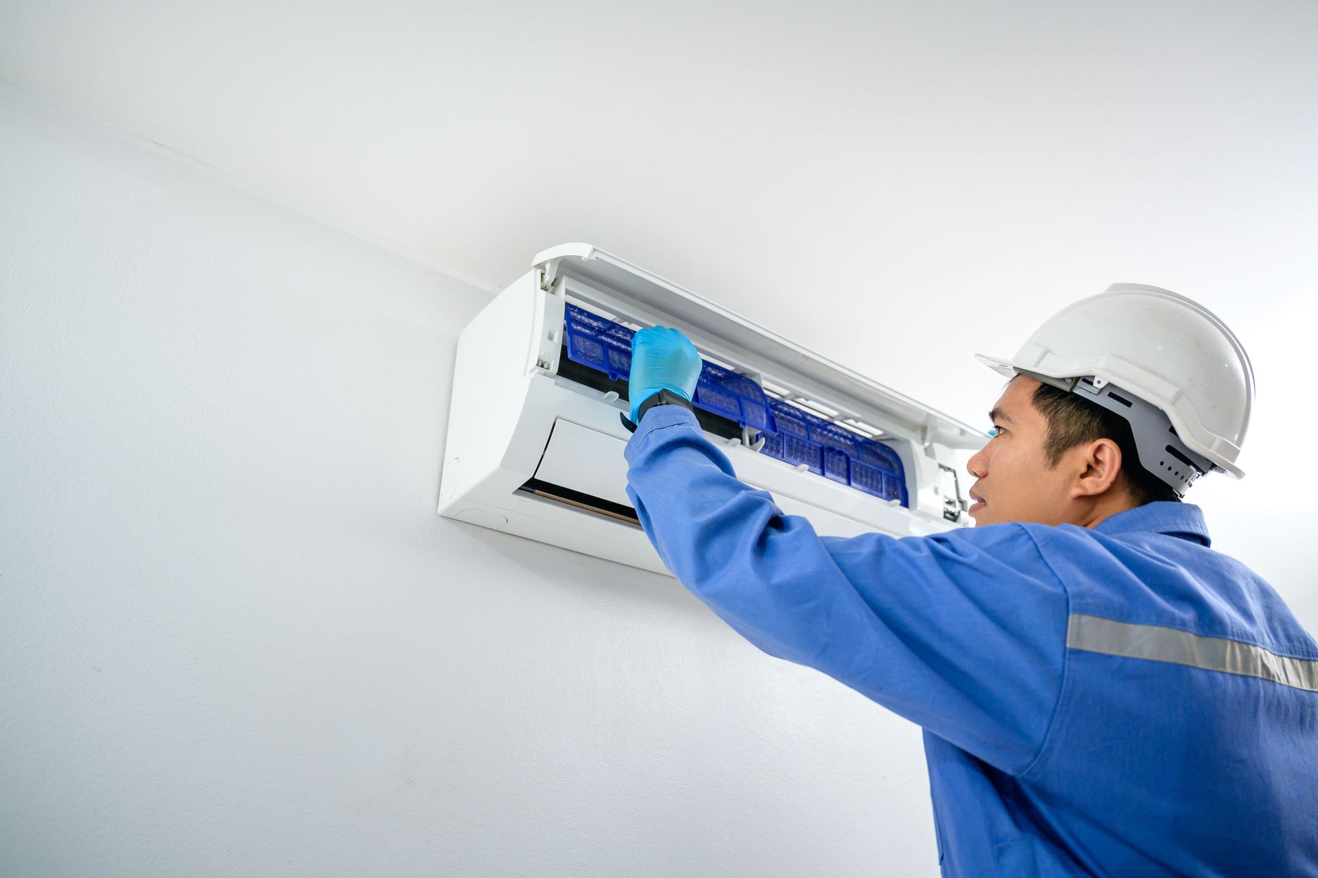 A professional technician performs an air conditioning installation on a modern wall-mounted unit A professional technician performs an air conditioning installation on a modern wall-mounted unit