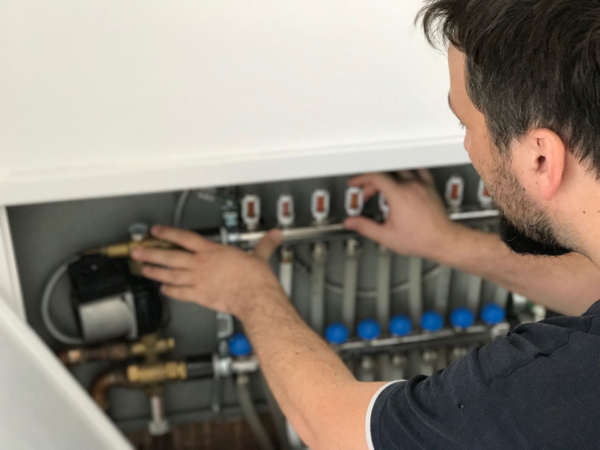 A person adjusts the controls on a radiant floor heating manifold inside a white cabinet.