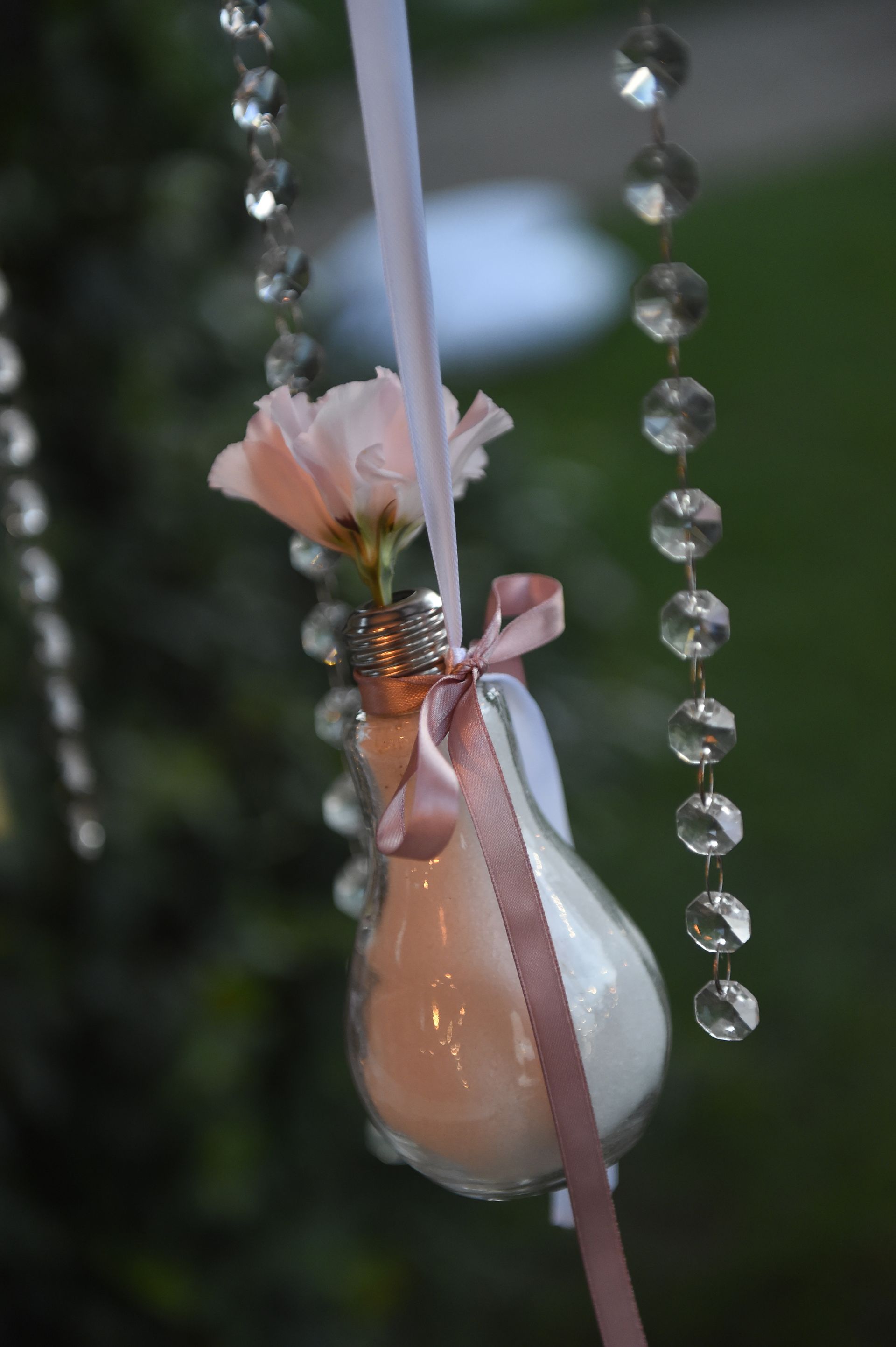 Da un filo di cristalli pende una lampadina con un fiore al suo interno.