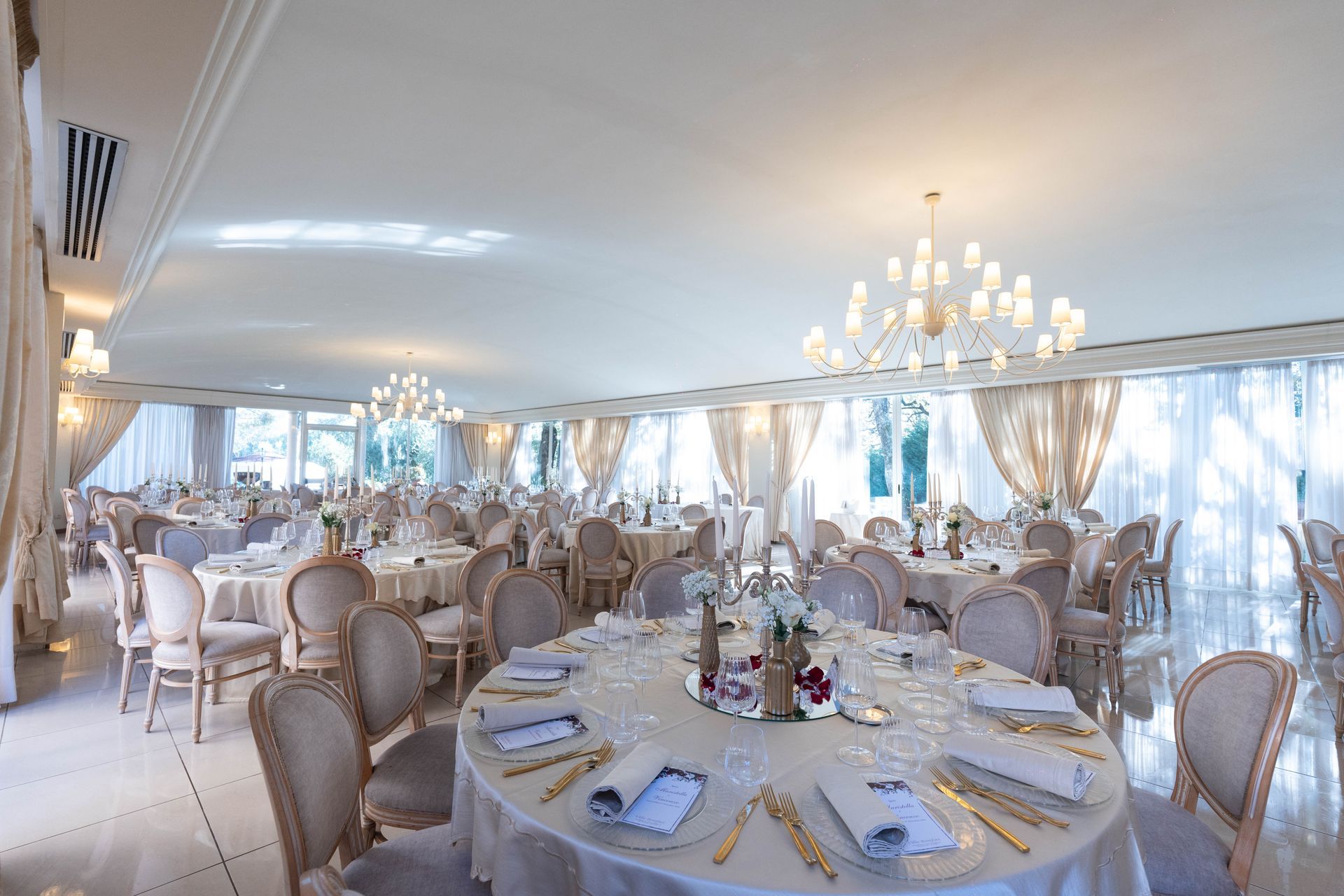 Una grande sala con tavoli e sedie allestita per un ricevimento di nozze.