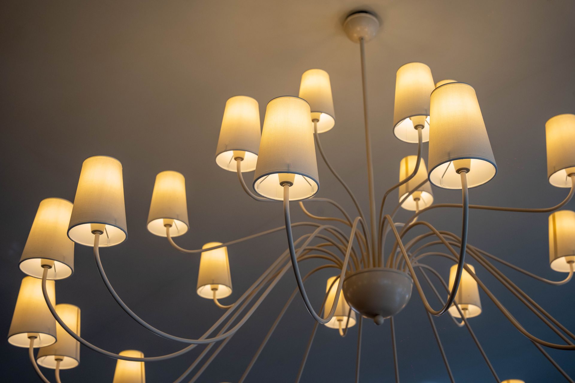 Dal soffitto pende un lampadario bianco con paralumi bianchi.