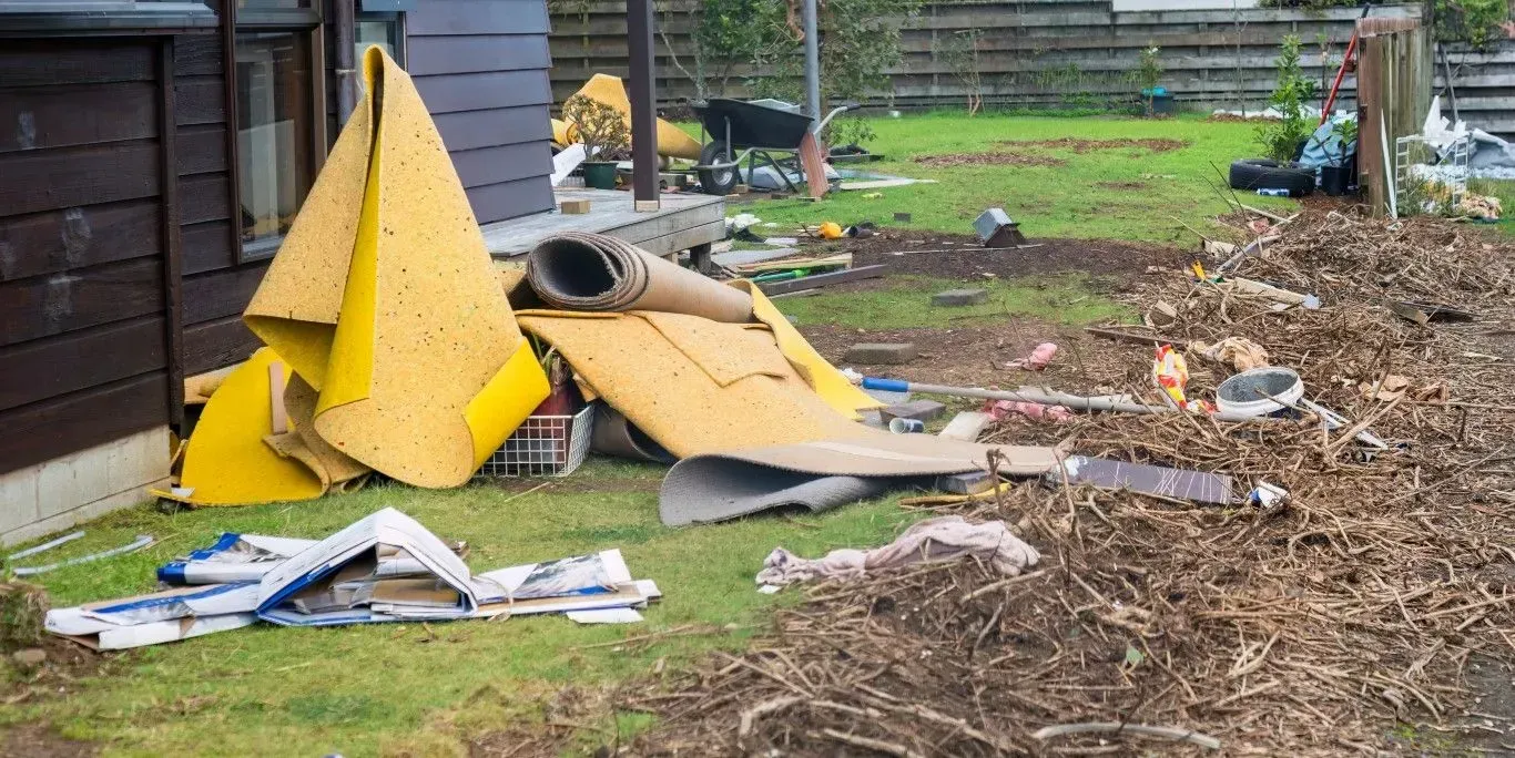 Collapsed yellow tarp or tent debris in a messy backyard beside a shed, with scattered trash and boards.