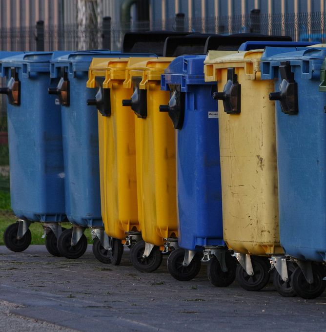 Row of colorful wheeled trash bins lined up outdoors on pavement