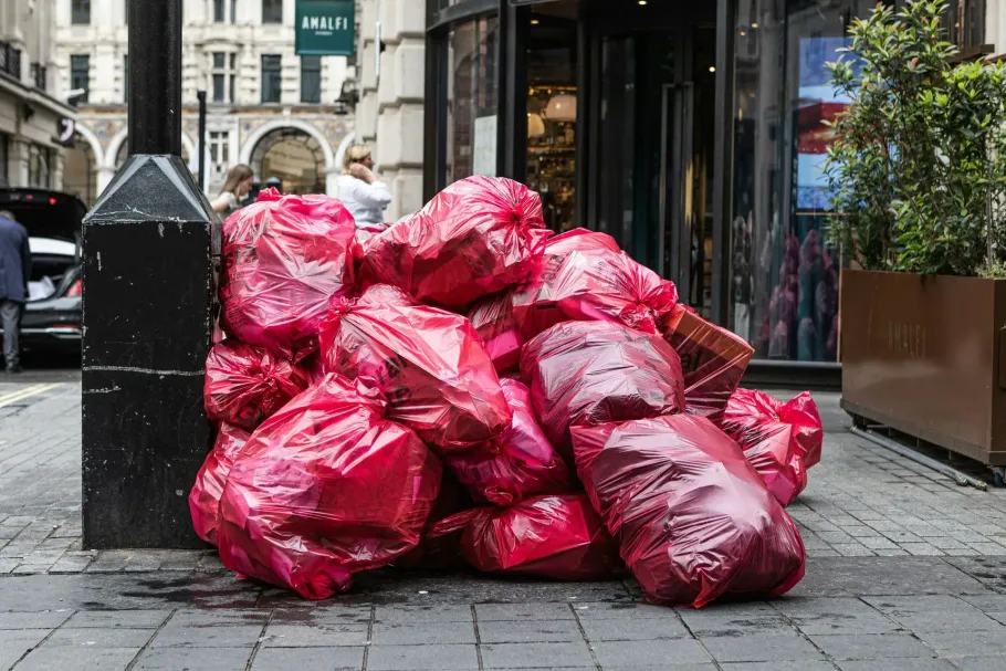 Pile of red trash bags piled on a city sidewalk outside storefronts