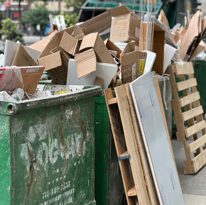 Overflowing green dumpster filled with cardboard boxes and scrap wood on a street