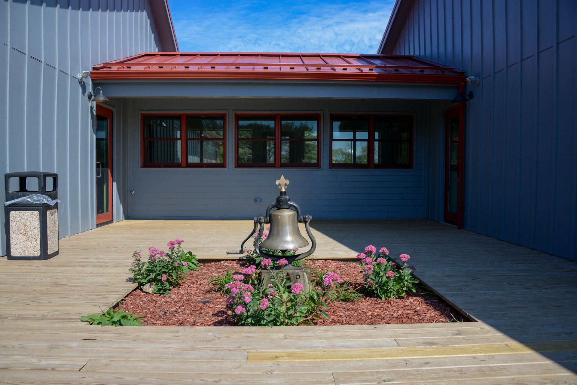 A bell is in the middle of a garden in front of a building.