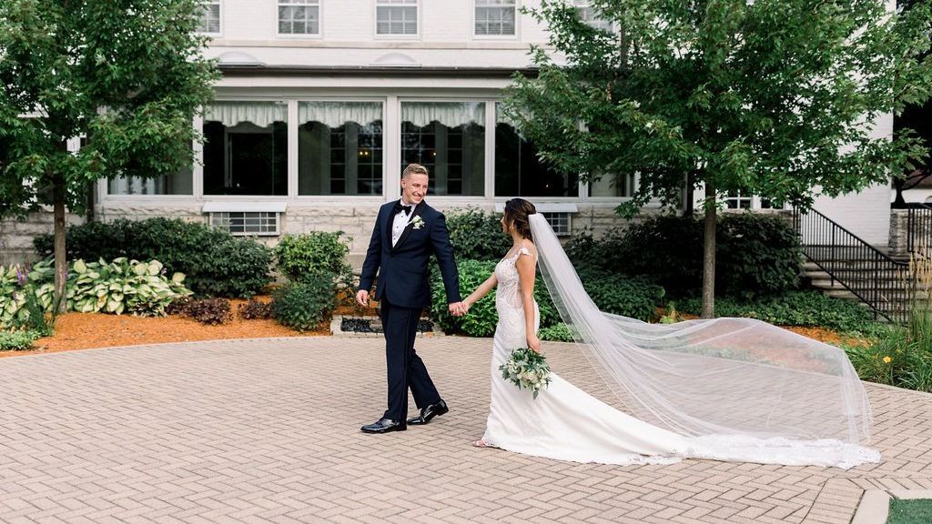 A bride and groom are holding hands in front of a large white house.