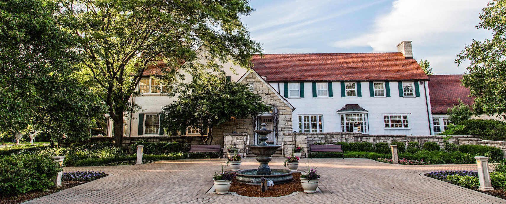A large white house with a red roof and a fountain in front of it.