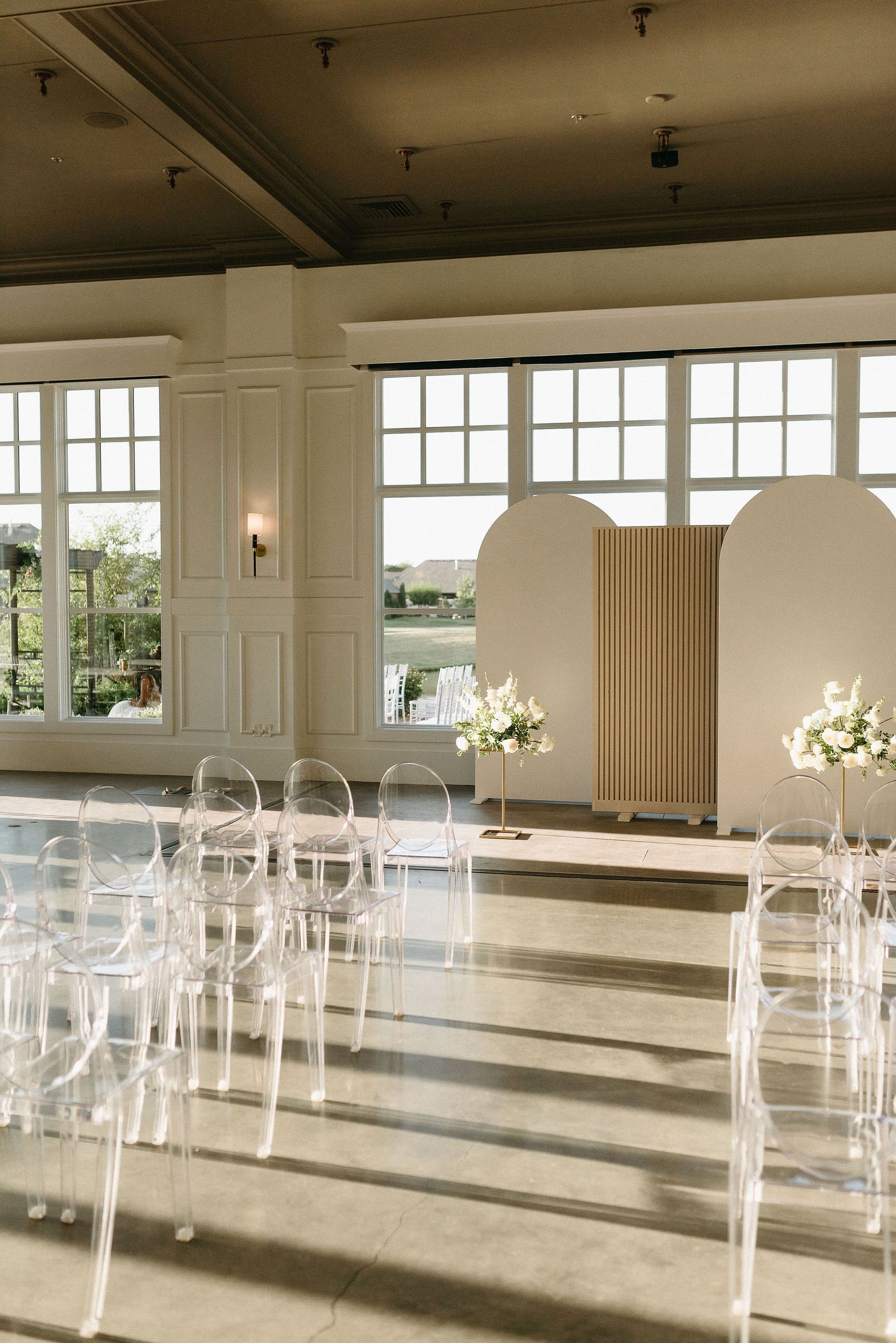 A room filled with clear chairs and flowers for a wedding ceremony.