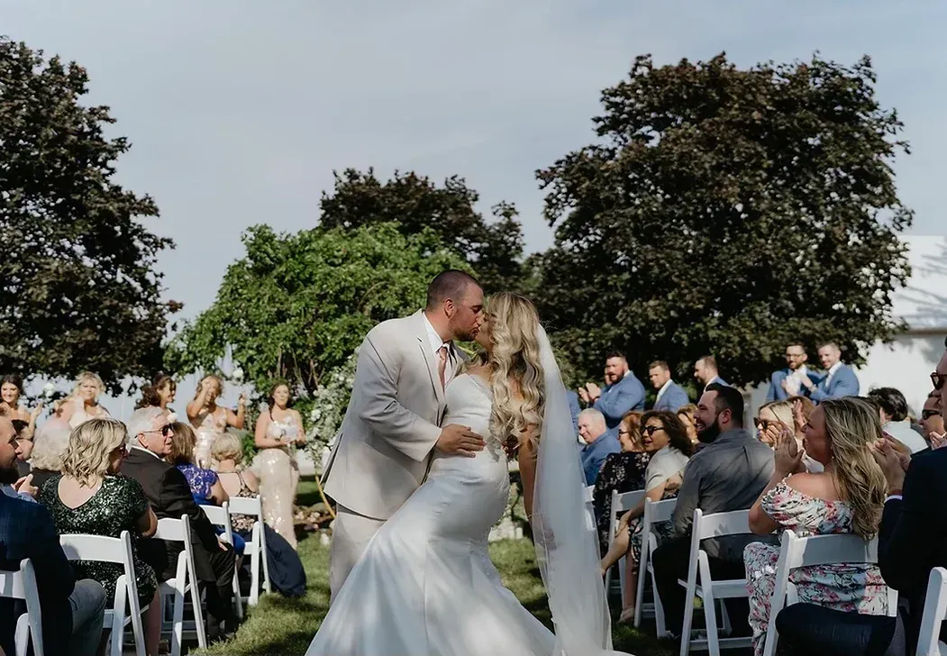 A bride and groom are kissing in front of their wedding guests.
