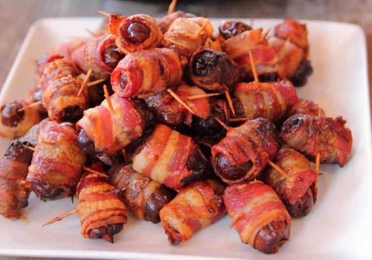 A white plate topped with bacon wrapped dates on toothpicks.