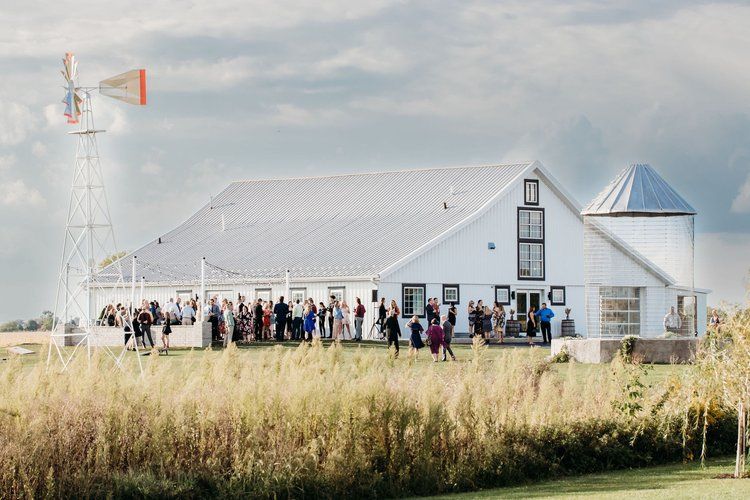 A group of people are standing in front of a white barn with a windmill in the background.