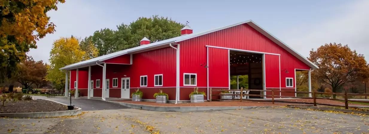 A large red barn with a white roof is surrounded by trees.