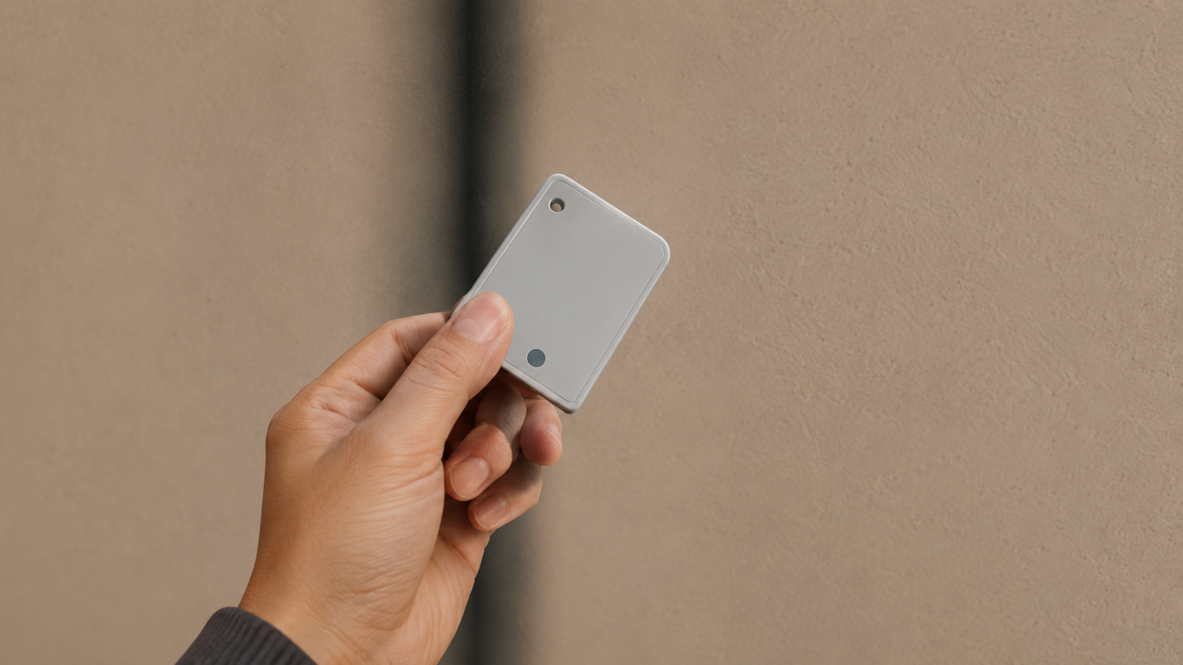 Hand holding a small white device against a plain beige background